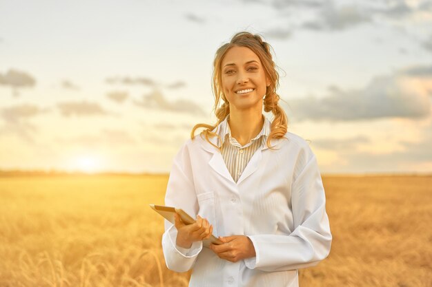 여자 농부 흰색 코트 스마트 농업 서 농지 디지털 태블릿을 사용 하여 웃 고