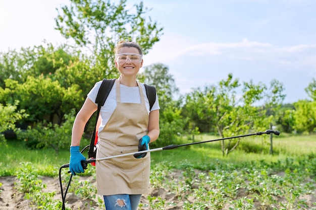 Woman farmer with backpack hand sprayer protecting young potato plants from colorado potato beetle pests and fungal diseases in spring vegetable garden