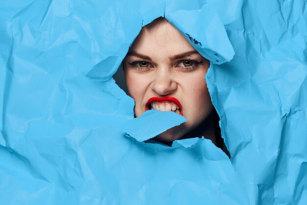 Woman fashion beauty portrait from torn colored blue paper parts of the face