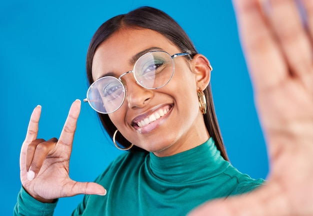 Woman fashion and selfie portrait with rock on hand for gen z attitude on blue background with glasses face of happy model person in studio with smile or cool sign emoji for beauty and motivation