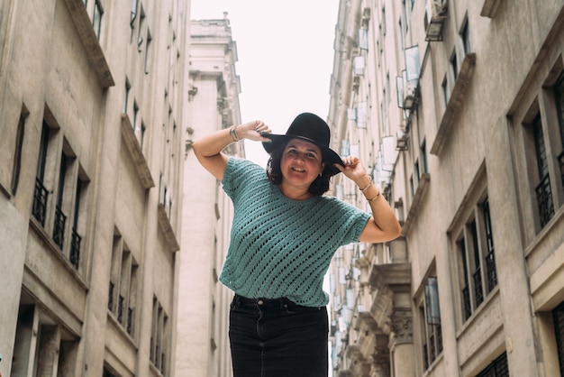 Woman in fashionable black hat looks and smiles at camera with a background of old architecture buildings