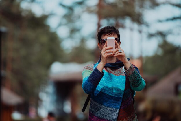 美しい晴れた日に公園で時間を過ごしながら、スマートフォンを使ってファッショナブルな服装をした女性。