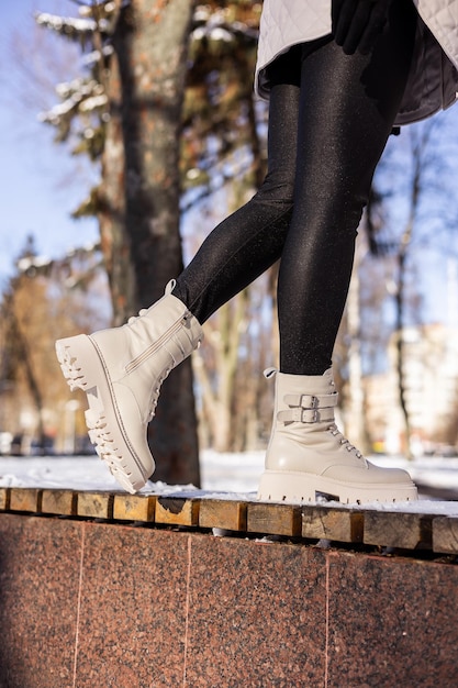 Woman in fashionable white boots on white snow closeup Womens legs in stylish winter leather boots