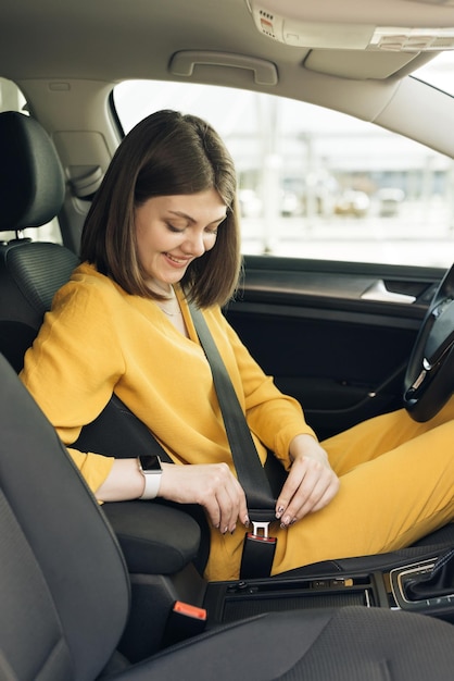 女性は女性の運転保護のための安全規則を手で遵守して車のシートベルトを締めます