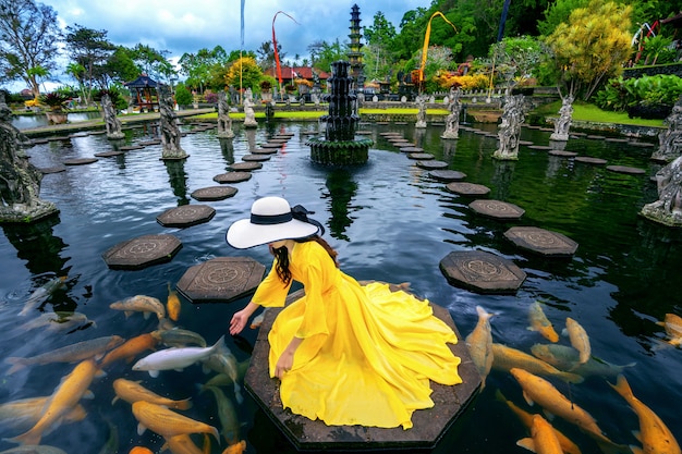 Photo woman feeding colorful fish in pond at tirta gangga water palace in bali, indonesia.