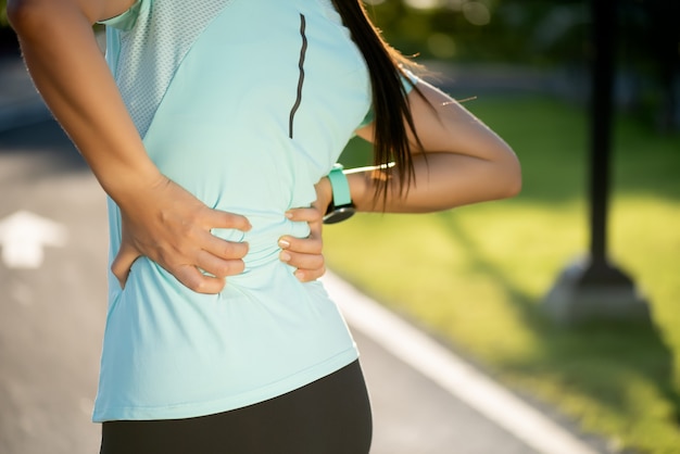 女性は運動、ヘルスケアの概念中に彼女の背中と腰に痛みを感じます。