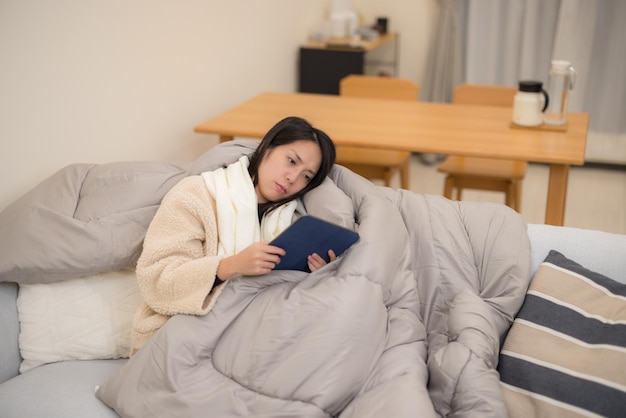 Woman feel sick lying on the couch and read on tablet computer at home