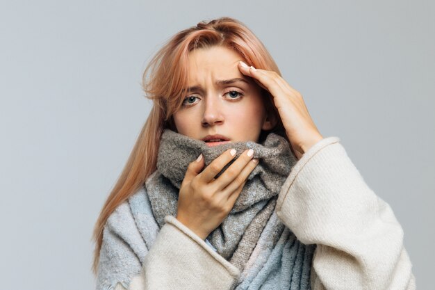 Woman feeling the first symptoms of flu, wrapped in a warm scarf