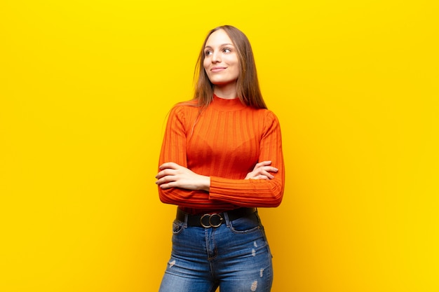 Woman feeling happy, proud and hopeful, wondering or thinking, looking up to copy space with crossed arms