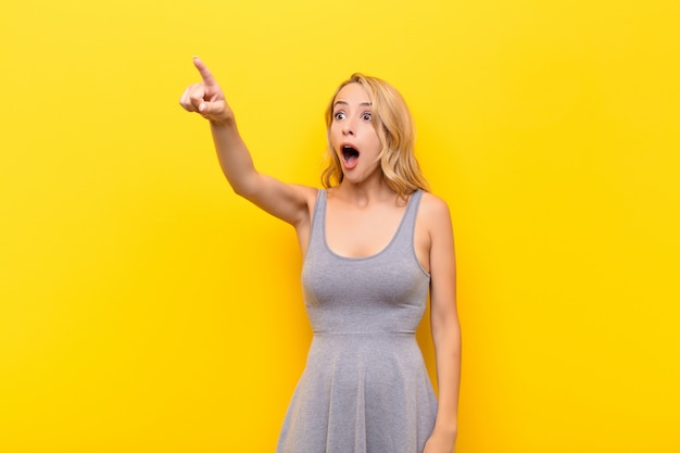 woman feeling shocked and surprised, pointing and looking upwards in awe with amazed, open-mouthed look