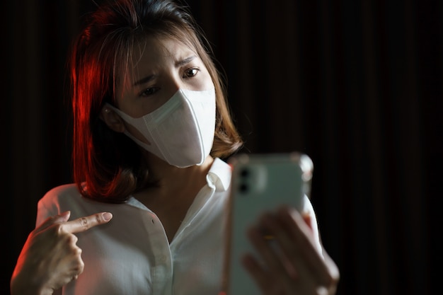 Woman feeling sick wearing protective mask corona virus (covid-19) text written use smart phone, worried about the news of the corona virus.