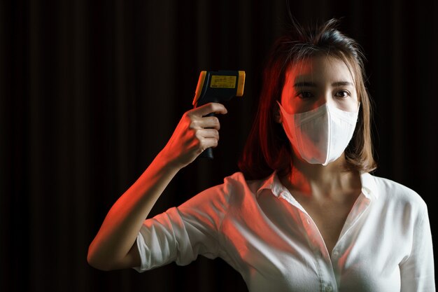 Donna che si sente male indossando maschera protettiva, uso della mano termometro digitale controllo temperatura.