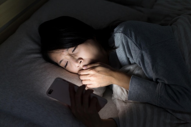 Woman feeling tired and using mobile phone on bed