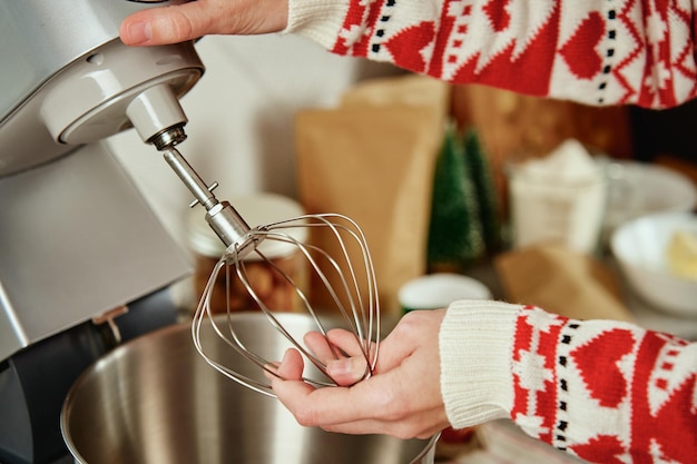 Woman in festive christmas sweater preparing dough for cookies at home kitchen female hands use elec