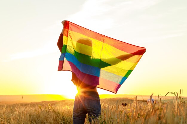 Donna nel campo che tiene la bandiera arcobaleno lgbt nel sole della sera del tramonto dorato