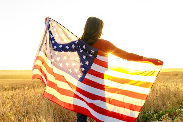 Woman in field holding USA stars and stripes flag in golden sunset evening sunshine