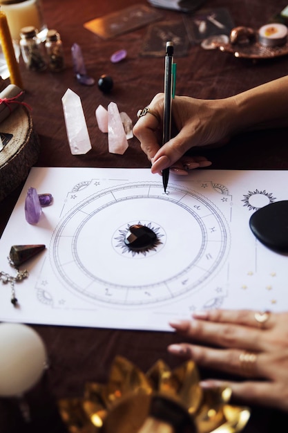 A woman fills in the zodiac symbols in a person\'s birth chart\
on her witch altar with autumn colors