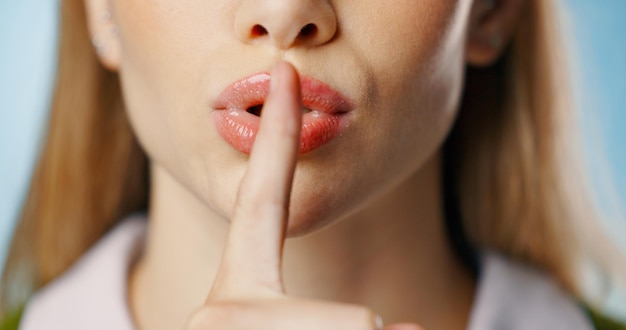 Woman finger and lip in studio for secret news and gossip for privacy with hand gesture for announcement on blue background Silence whisper emoji and confidential information shush and mystery