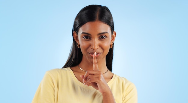 Woman finger to lips and secret in portrait with gossip news or announcement on blue background silence gesture and emoji in studio whisper for privacy and confidential information with sign