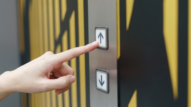 建物の中のエレベーターボタンの上ボタンを押す女性の指。