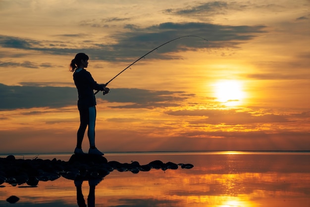 Woman fishing on Fishing rod spinning at sunset background