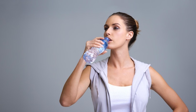 woman fitness and drinking water for hydration or natural sustainability on a gray studio background face of thirsty female person or athlete with mineral drink in rest break or recovery on mockup