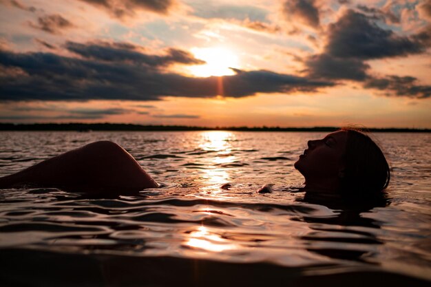 Foto donna che galleggia nelle onde al tramonto