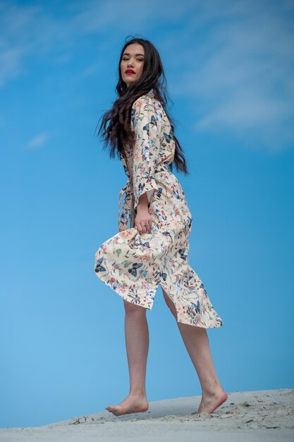 A woman in a floral dress stands on a blue background.