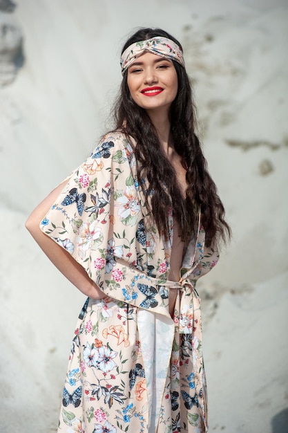 A woman in a floral dress stands in front of a white wall.