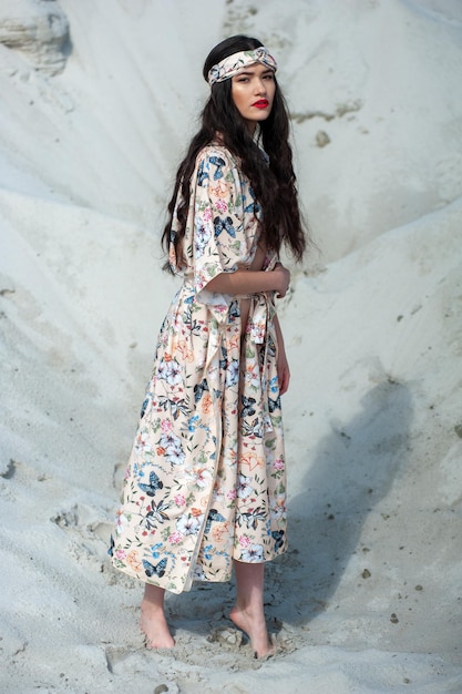 A woman in a floral dress stands in the sand.