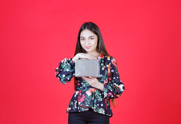 woman in floral shirt holding a silver gift box. 