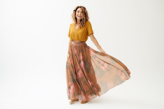 A woman in a floral skirt stands in a studio.