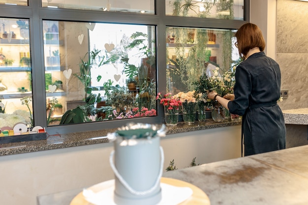 女性の花屋は花の花束を作成するために花を選びます。お祝いの贈り物としてのフラワーボックス。オリジナルギフトのコンセプト。