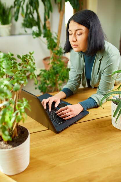 Woman florist with potted plant works on a laptop in flower plant shop