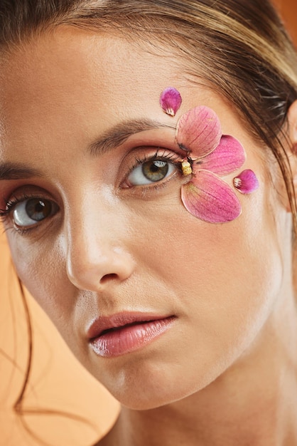 Woman flower and beauty eye makeup in portrait for cosmetics skincare and facial wellness mockup in studio against orange background Model cosmetic art and orchid petals design for spring