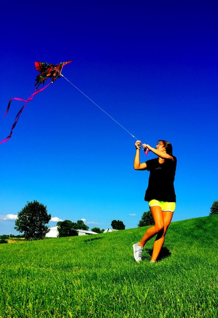 Woman flying kite against clear blue sky