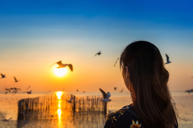 Woman flying over sea against sky during sunset