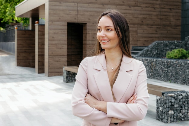 La donna ha piegato le mani e sorride in piedi sullo sfondo di un edificio per uffici