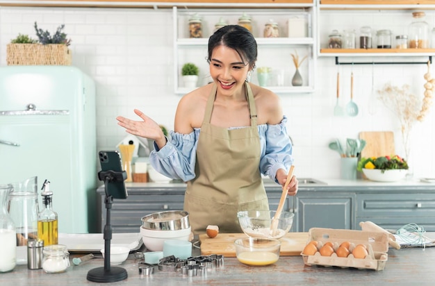 woman food blogger cooking cake in front of smartphone camera while recording vlog video in kitchen