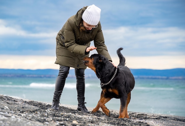 Woman fooling around with rottweiler dog in cold weather on the beach