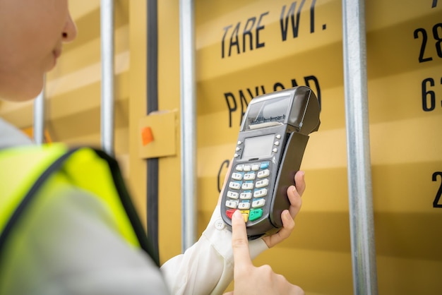 Photo woman foreman and operator using credit card swipe machine for checking code of cargo container before import exprot concept logistics transportation shipping lady foreman checking cargo warehouse