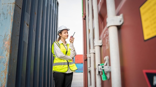 Женщина-бригадир улыбается с помощью рации перед грузовым погрузчиком на складе Менеджер в белом шлеме Супервайзер по безопасности в контейнерном таможенном терминале концепция порта импорт-экспорт
