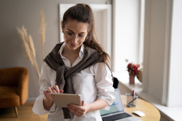 A woman formal attire in the office holding a tablet surfing the internet