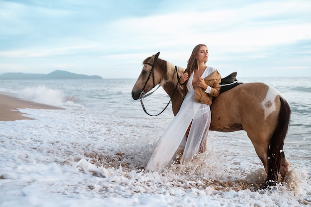 Woman in formal dress in ocean with horse, time exposure showing motion of waves 