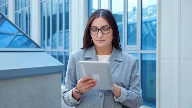 Woman in a formal suit and glasses looks into a tablet on the street