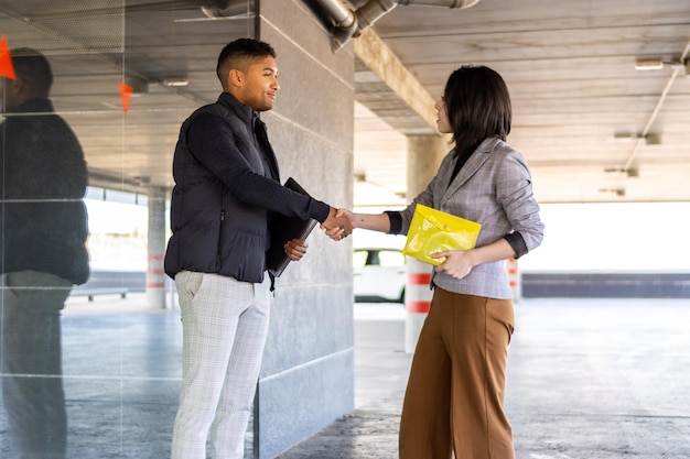 Woman in formal suit shaking hands with casual man outdoors Business woman shaking hands with guy on the street