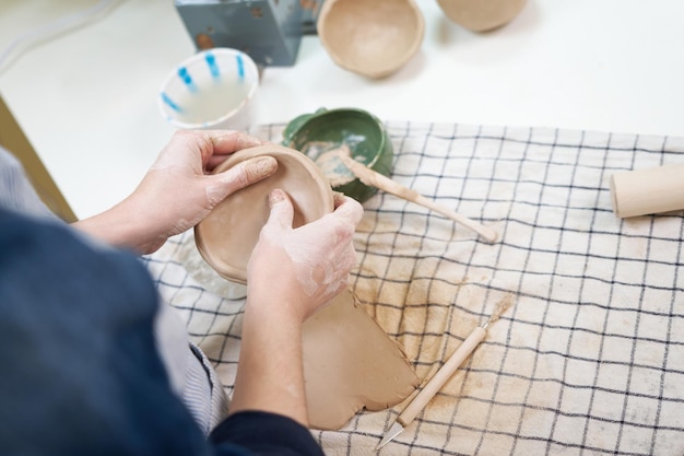 Woman forming clay pot shape by hands closeup in artistic studio