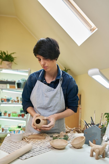 芸術的なスタジオでの手のクローズ アップによって土鍋の形状を形成する女性