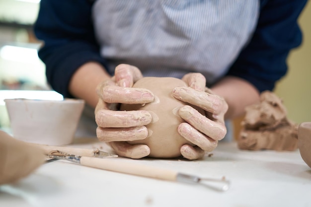 Женщина формирует форму глиняного горшка руками крупным планом в художественной студии
