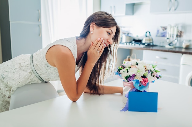 Woman found bouquet of flowers in gift box and envelope with card on kitchen. 